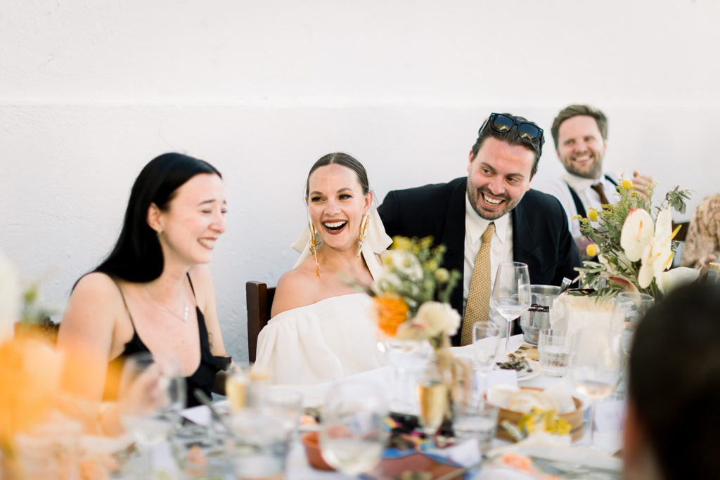 Bride and groom laughing with their wedding guests by the table